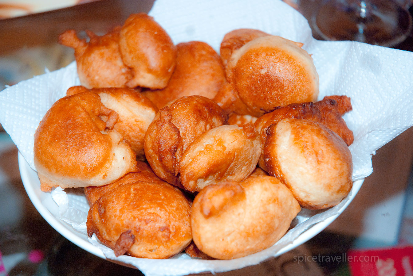 A bowl of freshly fried Mandazi fritters, a popular Ugandan snack, served with a sprinkle of powdered sugar