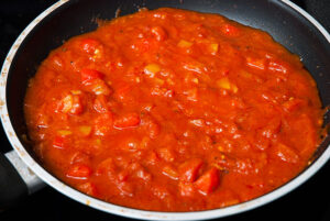 Fresh tomatoes and peppers sizzling in a pan, the foundation of a delicious shakshouka