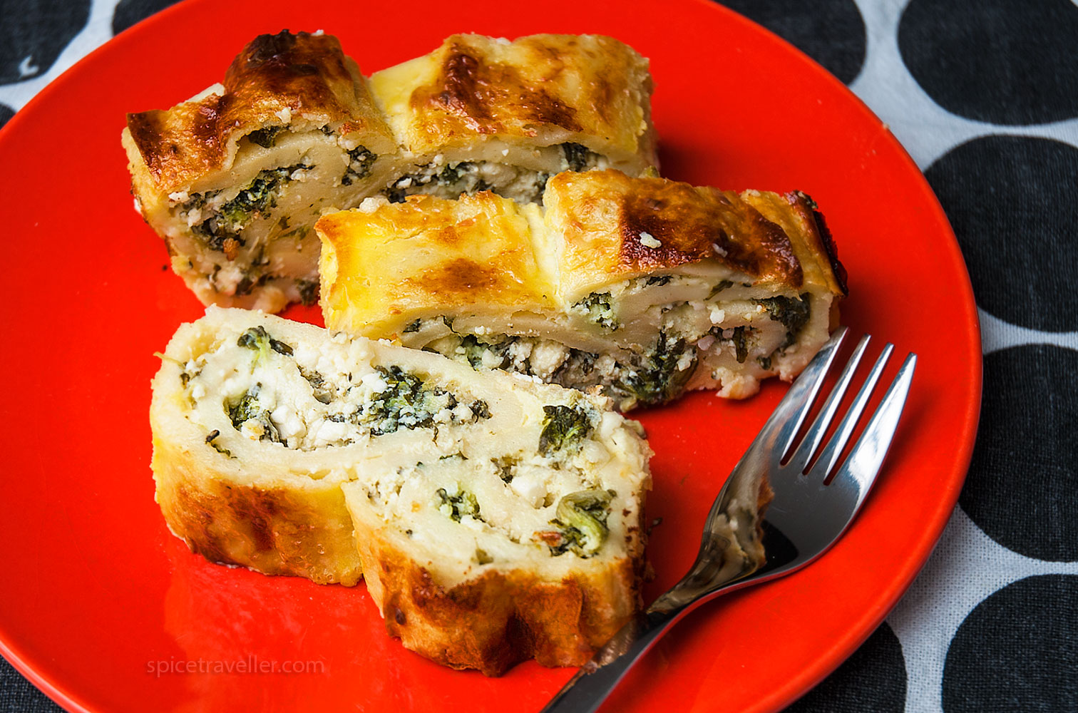 Croatian oven-baked pancakes with spinach and cheese slices on a red plate.