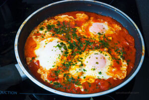 Close-up view of a vibrant and aromatic Shakshuka dish, featuring poached eggs in a rich tomato sauce, garnished with fresh herbs.
