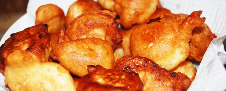 A close-up view of Mandazi fritters in a bowl, sprinkled with powdered sugar