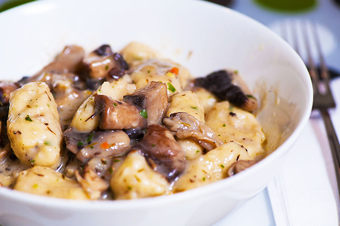 A bowl filled with mushroom and thyme gnocchi, generously coated with mushroom sauce, creating a delicious and visually appealing dish.