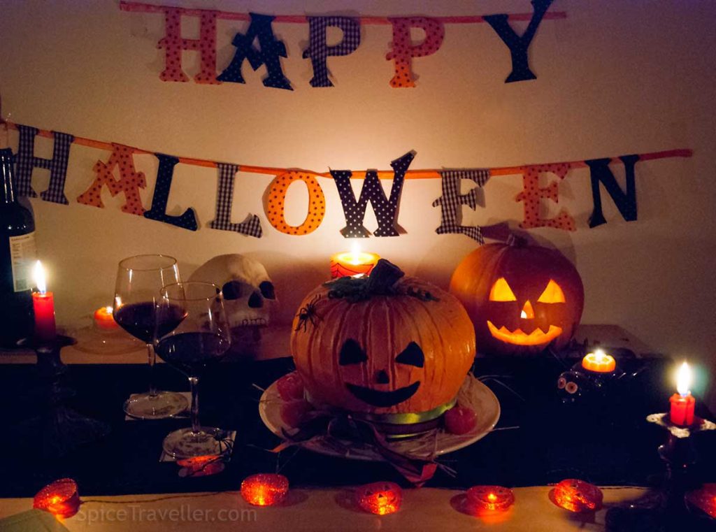 Halloween-themed dining table with lit candles, Jack-o-Lantern cake and glowing carved pumpkin cake. 