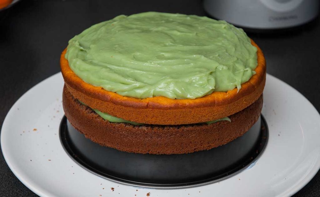 Assembling halloween pumpkin and chocolate sponge cake - added orange pumpking sponge layer and spread another layer of green cream.