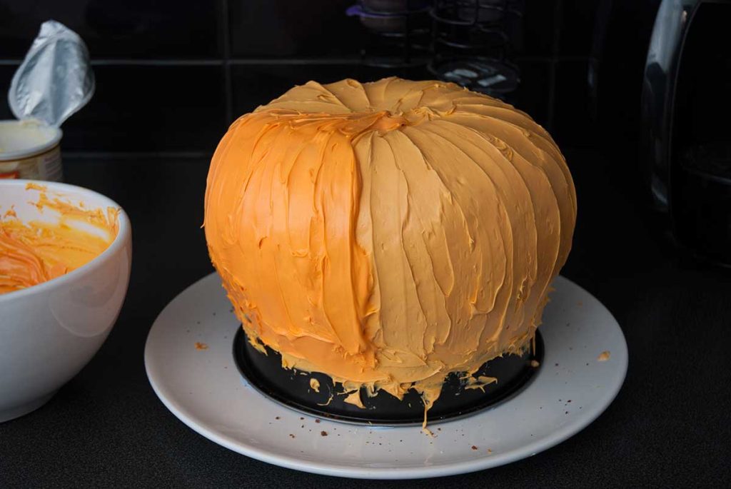 Covered cake with second level of icing and starting with the third and final decorative orange layer of icing.