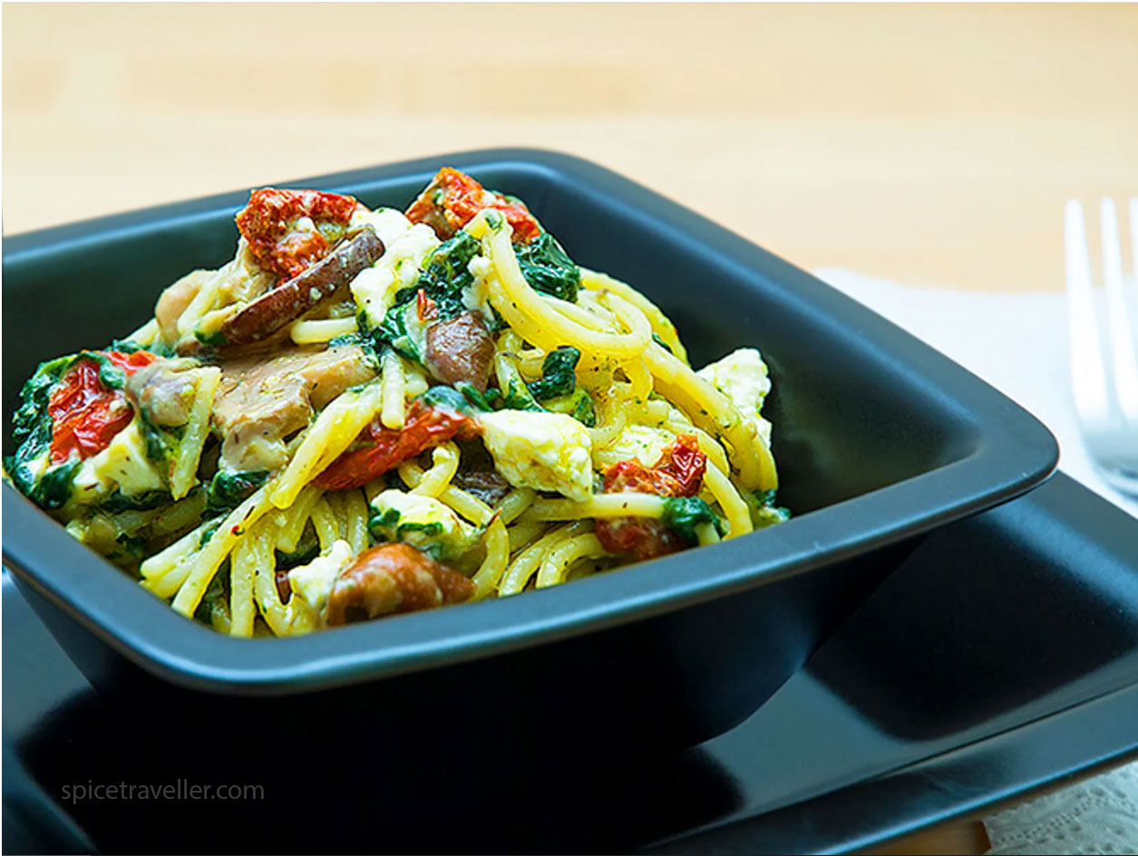 A bowl of vegetarian Mediterranean pasta spaghetti with sun-dried tomatoes, spinach, mushrooms, capers, and feta cheese