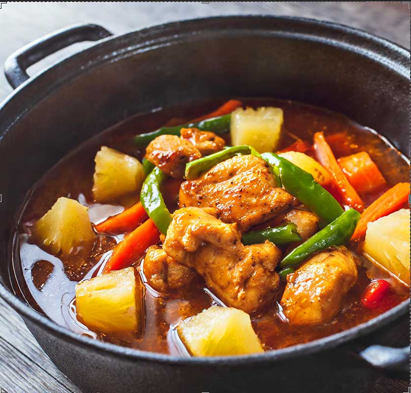 Chicken pieces cooking with peppers, carrots and pineapple in a thin sauce