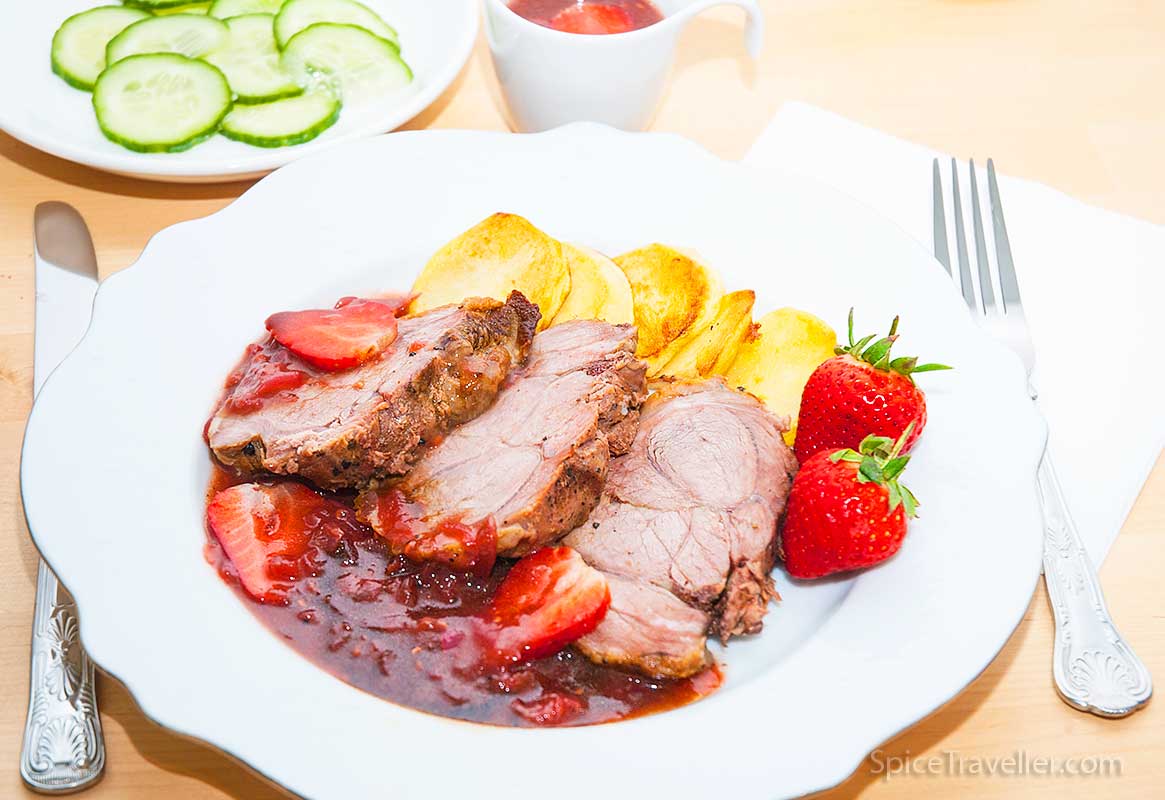 Plate with three slices of lamb roast served with sliced baked potato and delicious strawberry and balsamic sauce
