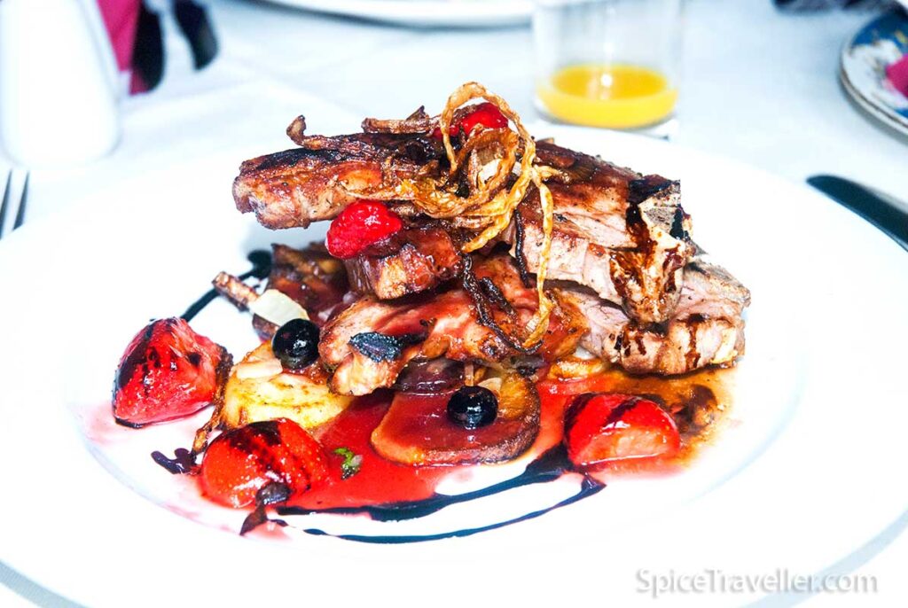 Three slices of roasted lamb served with sweet berry and balsamic sauce and decorated with a few sliced strawberries and blueberries.
