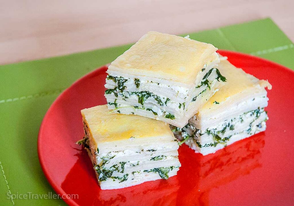 Greek spanakopita with pancakes, square portions on a red plate.