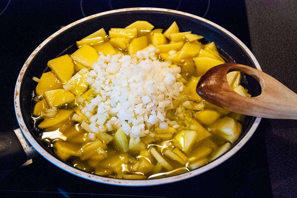 Chopped onions added to potatoes already frying in a pan