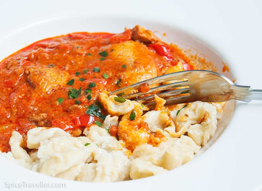 Close up of Hungarian Chicken paprikash served with dumplings ( nokeldi) in a white bowl