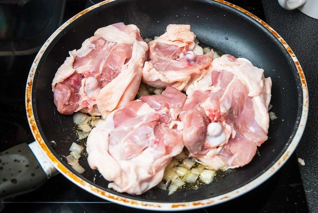 Chicken thighs frying ith copped onions in a pan , with the skin down.