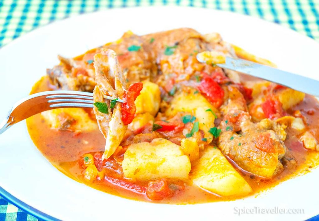 Close up of delicious Pollo Guisado chicken stew, with chicken piece on a fork.