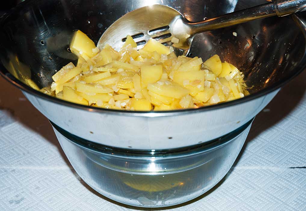 Draining potatoes and onions  in a metal sieve over glass bowl