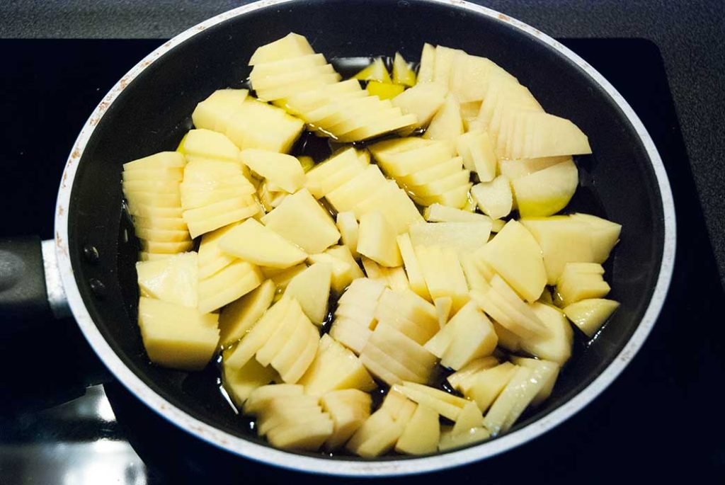 Sliced potatoes frying in a pan with lots of oil