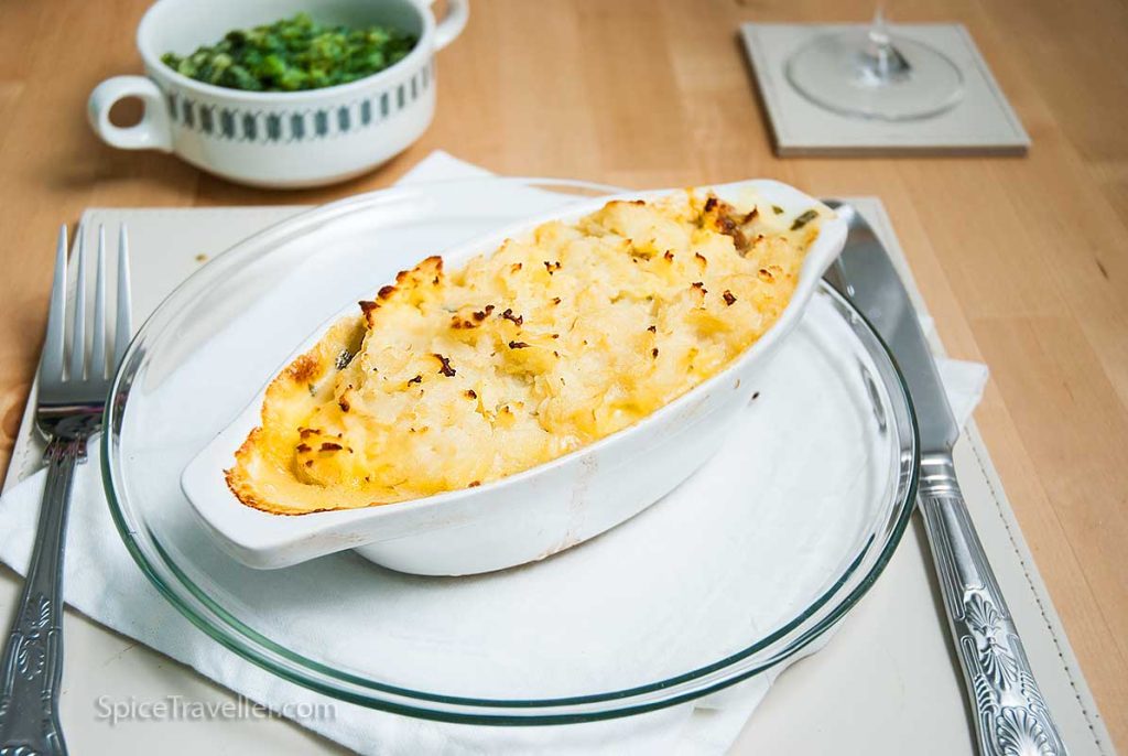 perfectly baked luxury seafood fish pie served in small oval white dish, alongside bowl of chard in elegant settings