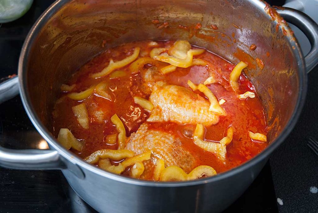 Preparing Hungarian Chicken Paprikash, mixing chicken pieces with pepper sauce.