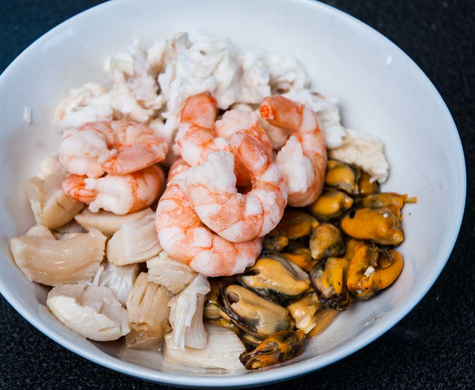 Cooked fmonkfish tail and shellfish in a white bowl