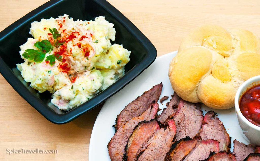 Spicy Texas-style potato salad served with sliced beef and a small bread roll.