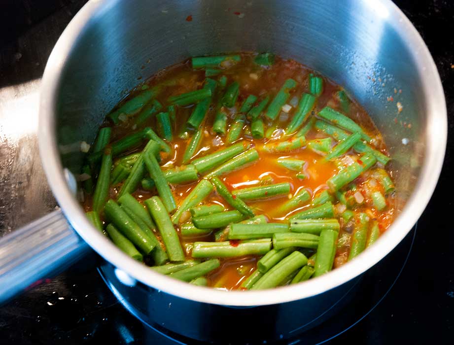 Green beans cooking in a pot with wine, water and paprika.