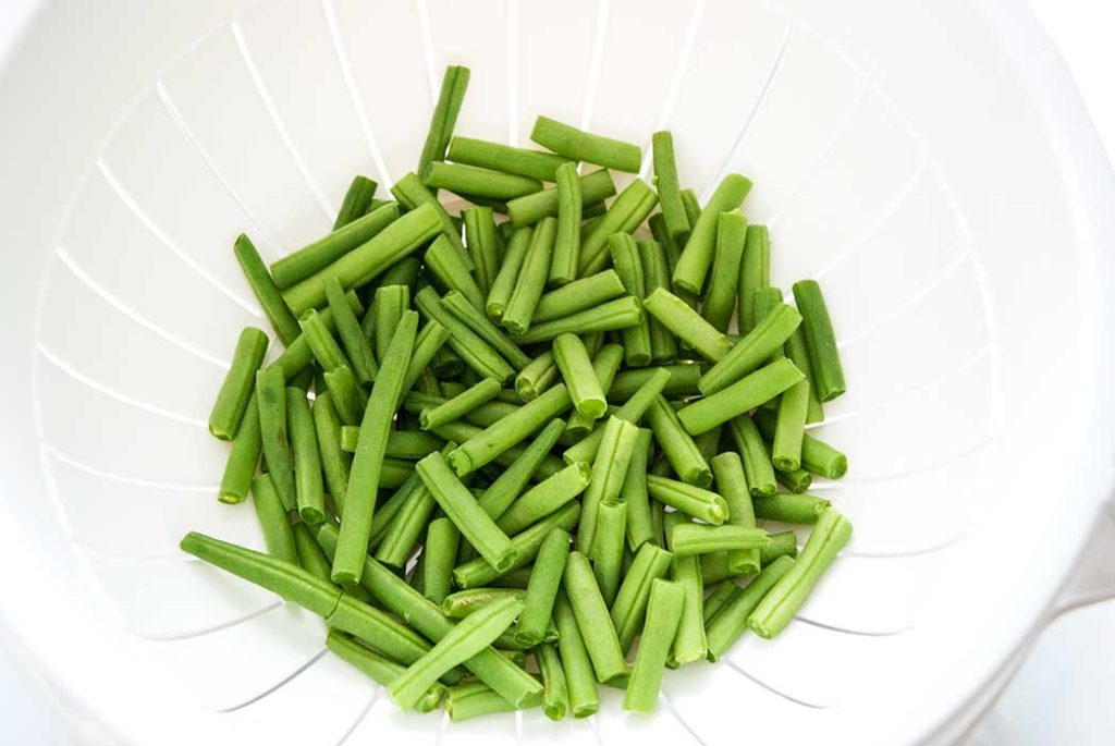 Fresh green beans chopped and washed draining on a white plastic sieve