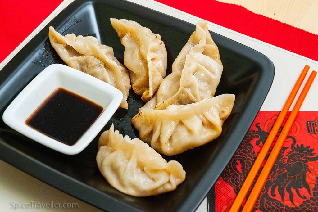 Four delicious pieces of Chinese dumplings served in a black rectangular bowl with a soy dipping sauce.