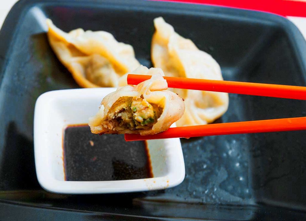 Close-up of a Chinese dumpling bitten in half, with the filling visible, and held by chopsticks.