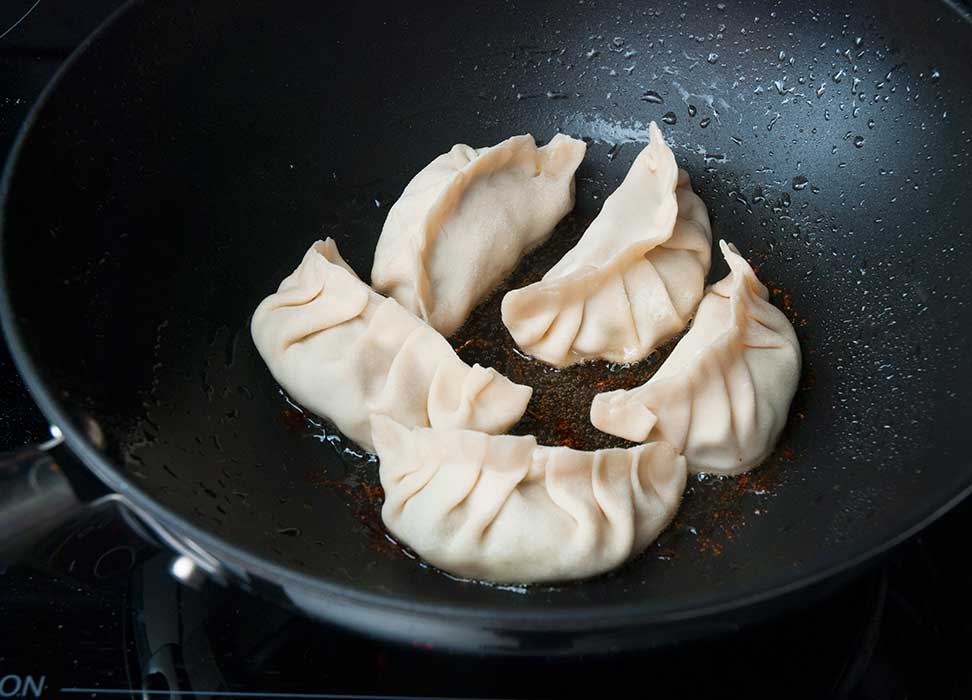 Chinese dumplings frying in a wok.