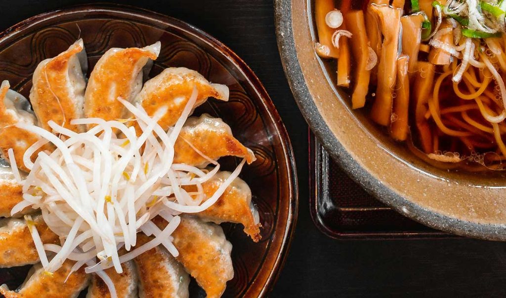 Chinese dumplings - potstickers served on a plate next to a bowl of noodle soup as a serving suggestion.