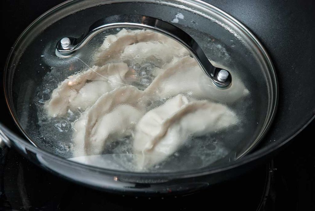 Step 2 - Fried Chinese dumplings steaming in little water in a wok, covered with a transparent lid.