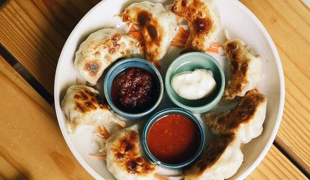 Chinese dumplings potsticker-style served on a plate with 3 different dips.