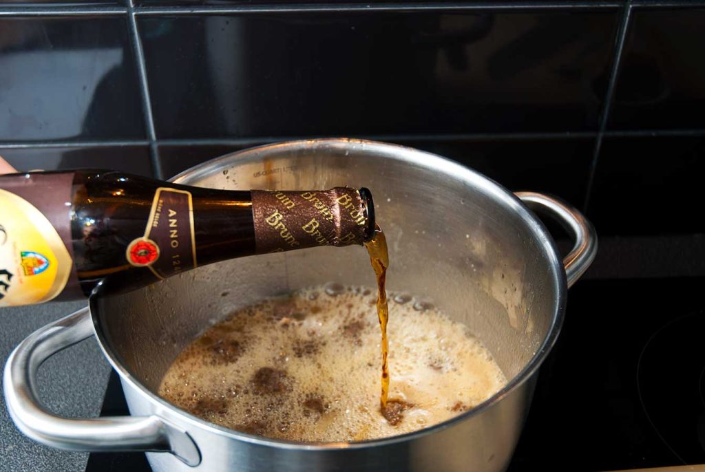 Pouring Belgian brown ale Leffe into the pot with onions and meatballs.