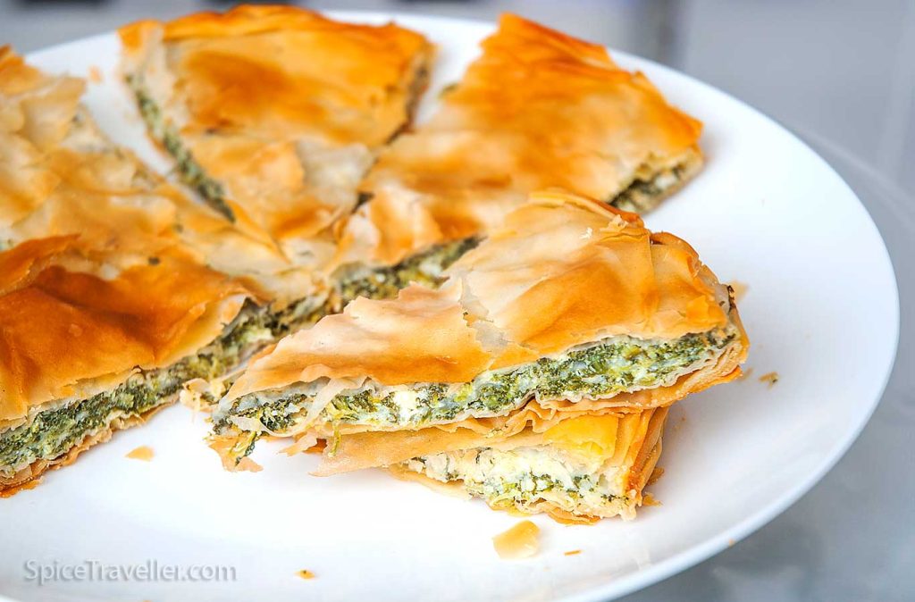 Round Albanian Börek, sliced into triangular pieces, showcasing layers of filo dough filled with spinach and cheese