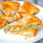 Round Albanian Börek, sliced into triangular pieces, showcasing layers of filo dough filled with spinach and cheese