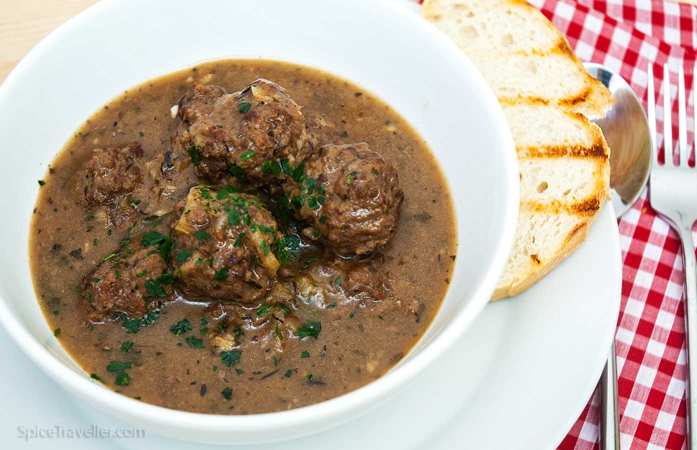 White bowl with Belgian beef stew meatballs served with a sliced toasted bread.