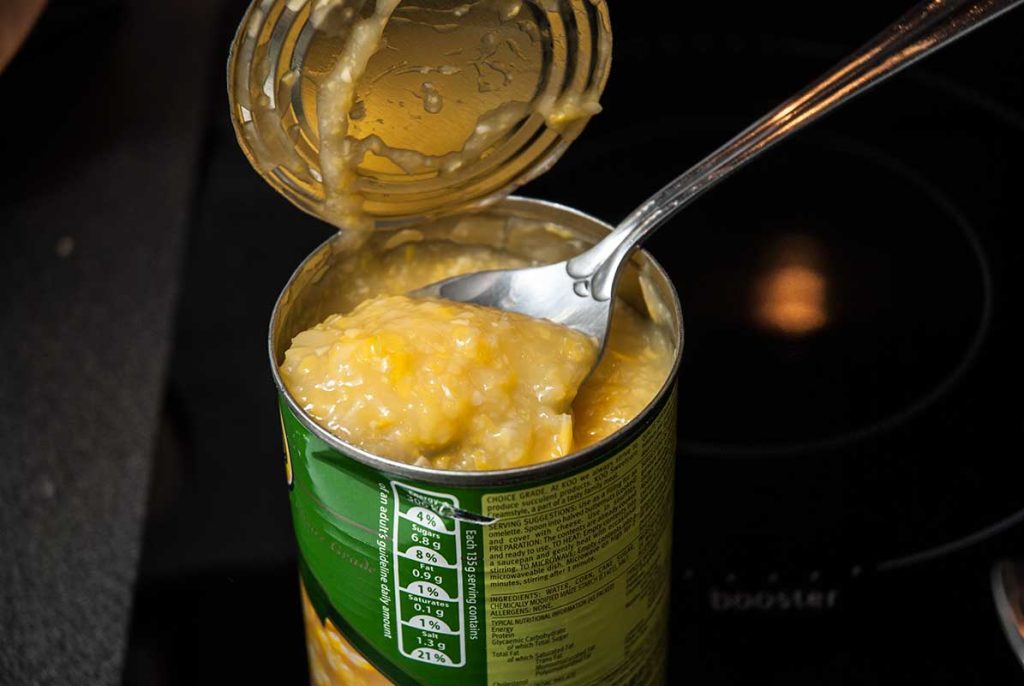 Taking creamed corn out of the can with a spoon.