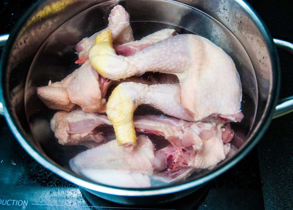 Add chicken pieces into a large pot and fill with water.