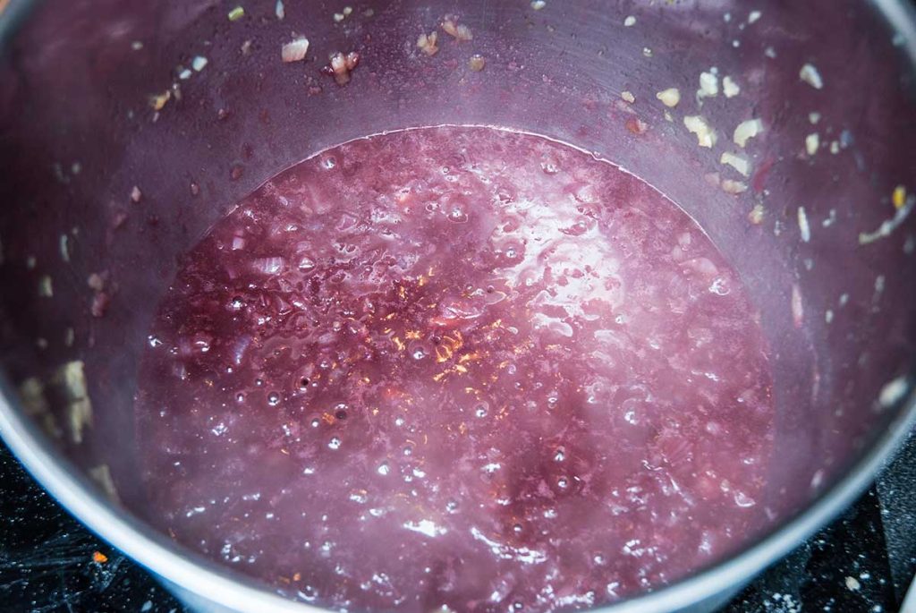 Gravy with red wine and onions cooking in a pot.