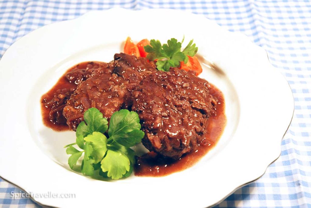 Deliious gourmet Salisbury Steak served on a playe with sliced tomato.