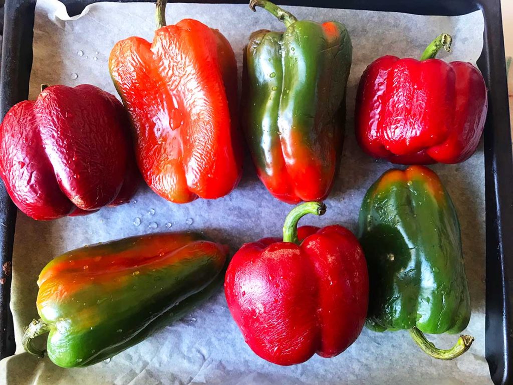 Fresh large colourful bells peppers on a baking tray ready to roast.