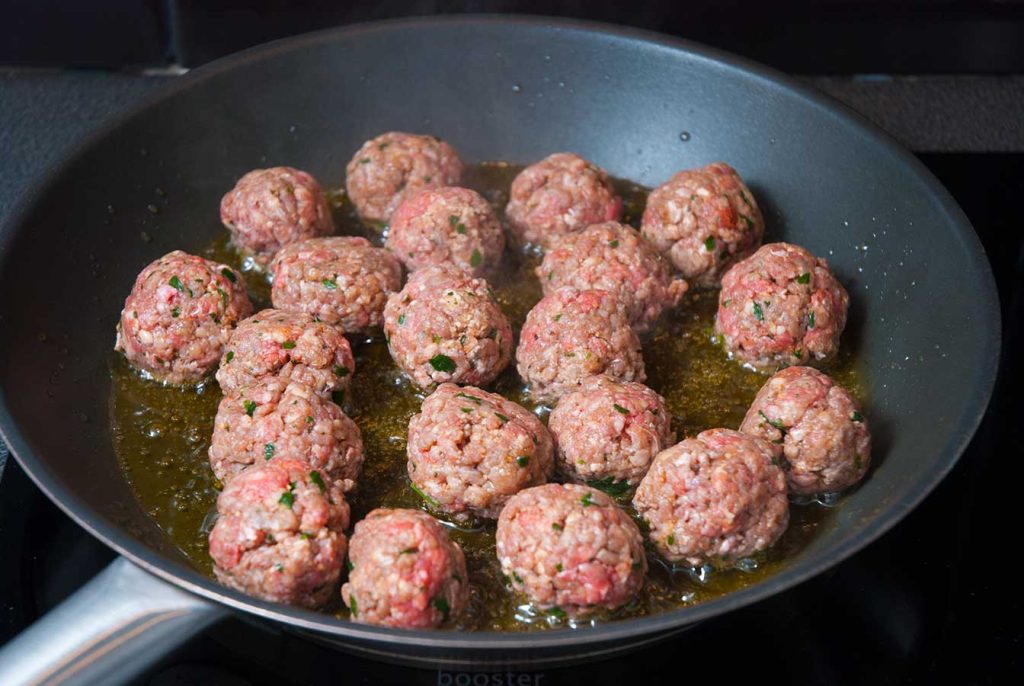 Beef meatballs frying in a pan.