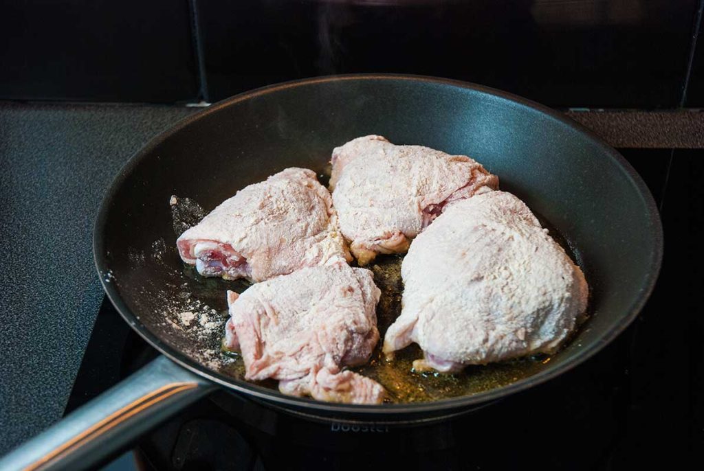 Floured chicken thighs frying in a pan.