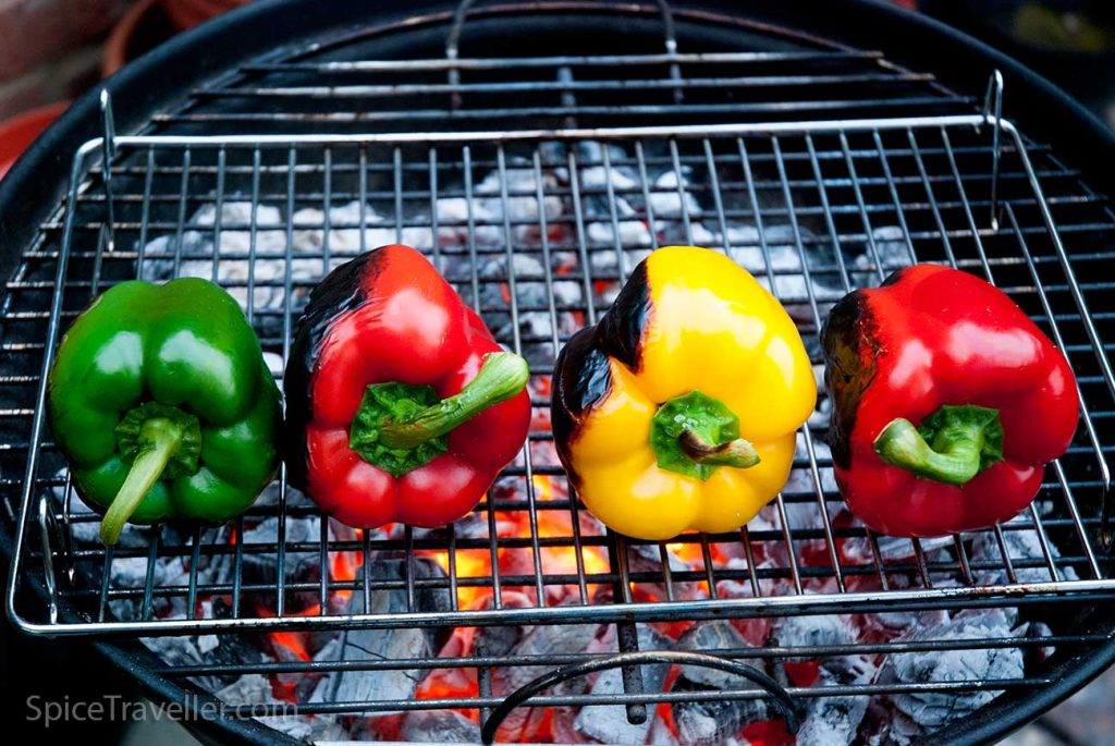 Four colourful bell peppers grilling on BBQ.