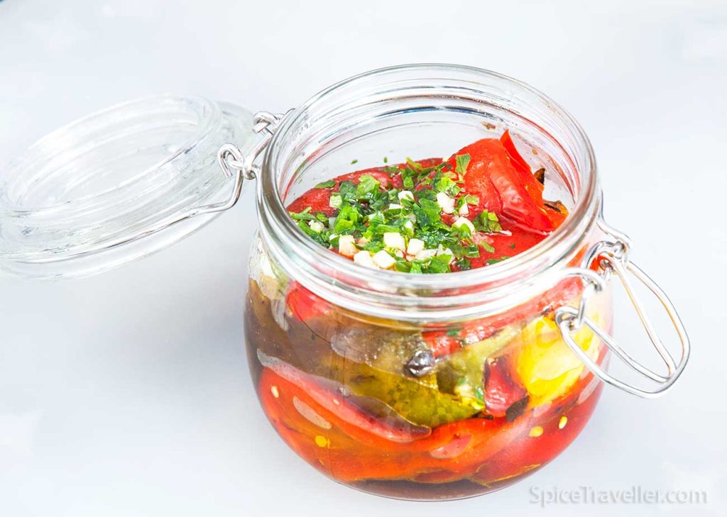 Small jar with colourful roasted bell peppers with a touch of chopped parsley and garlic.