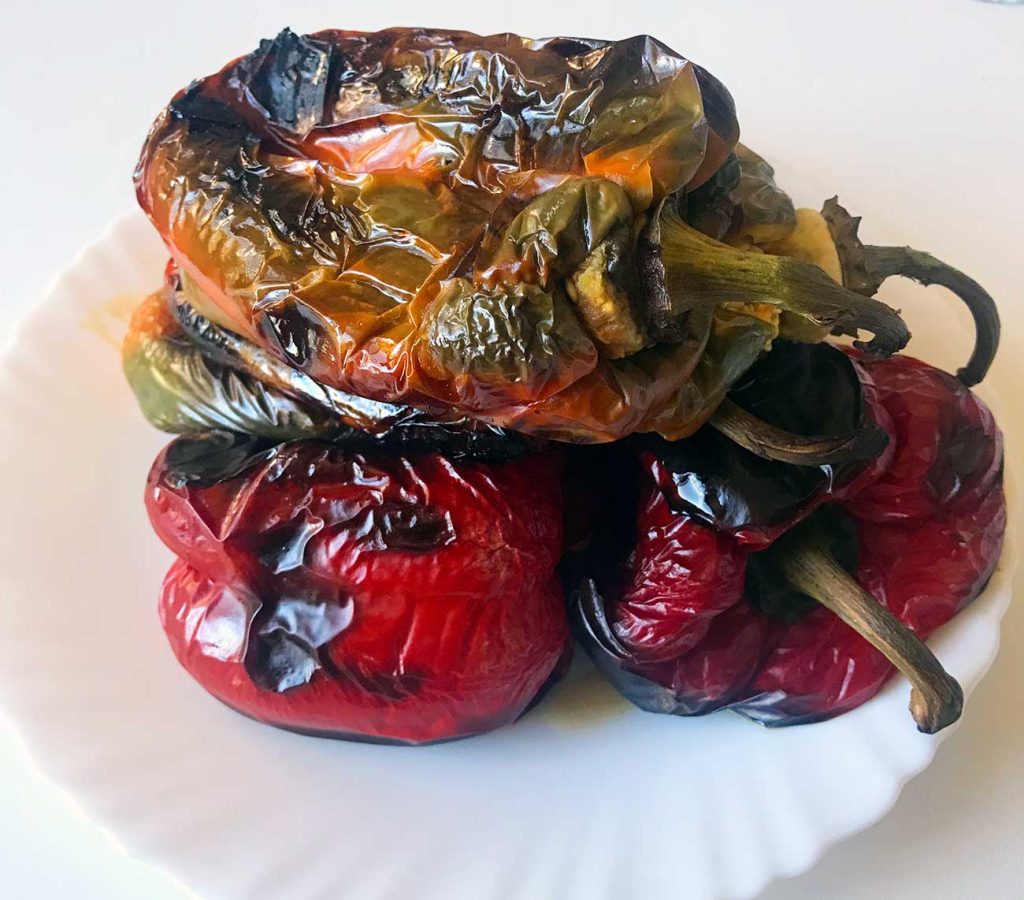 Roasted peppers resting in a bowl before skinning.