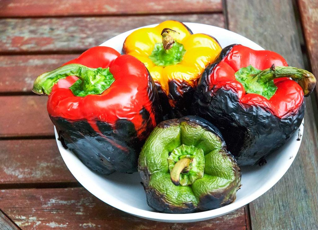 Grilled peppers in a white bowl resting before skinning and deseeding.