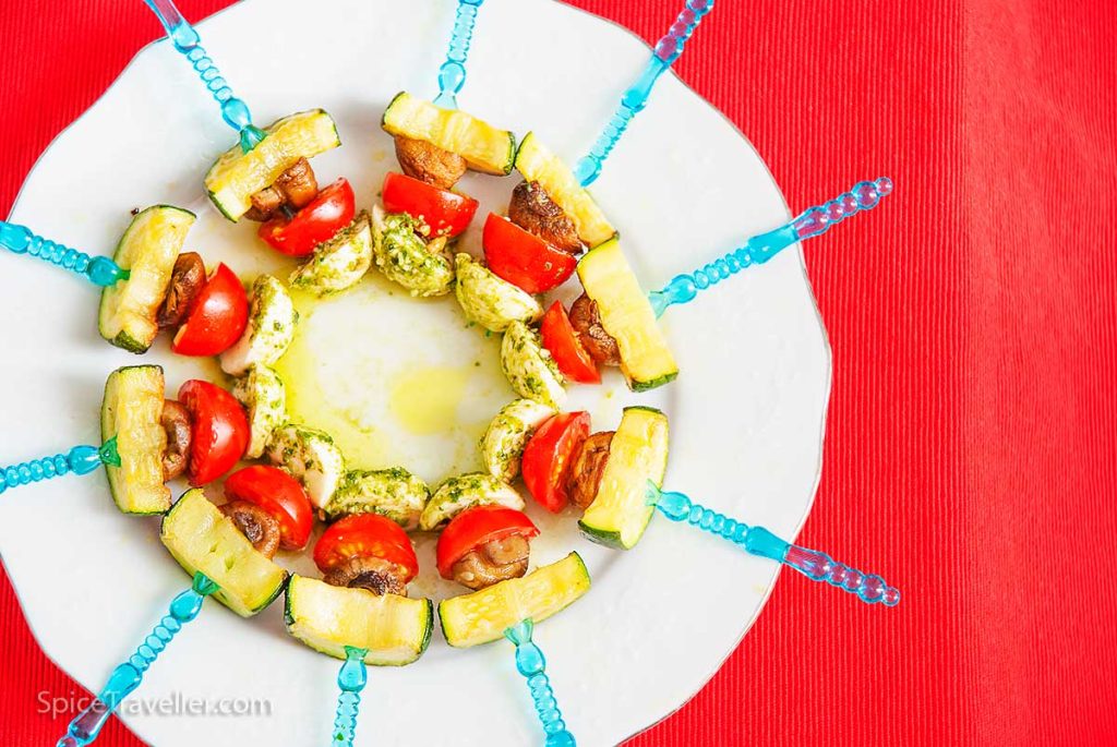 Monte Carlo roasted vegetable salad ingredients served as canapés on tiny plastic forks arranged in a circular pattern on a white plate.