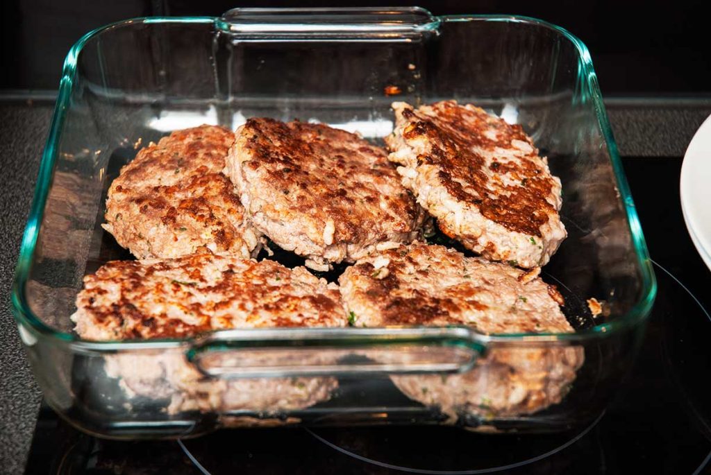 Fried beef burgers or patties in a baking dish ready to be topped with gravy.