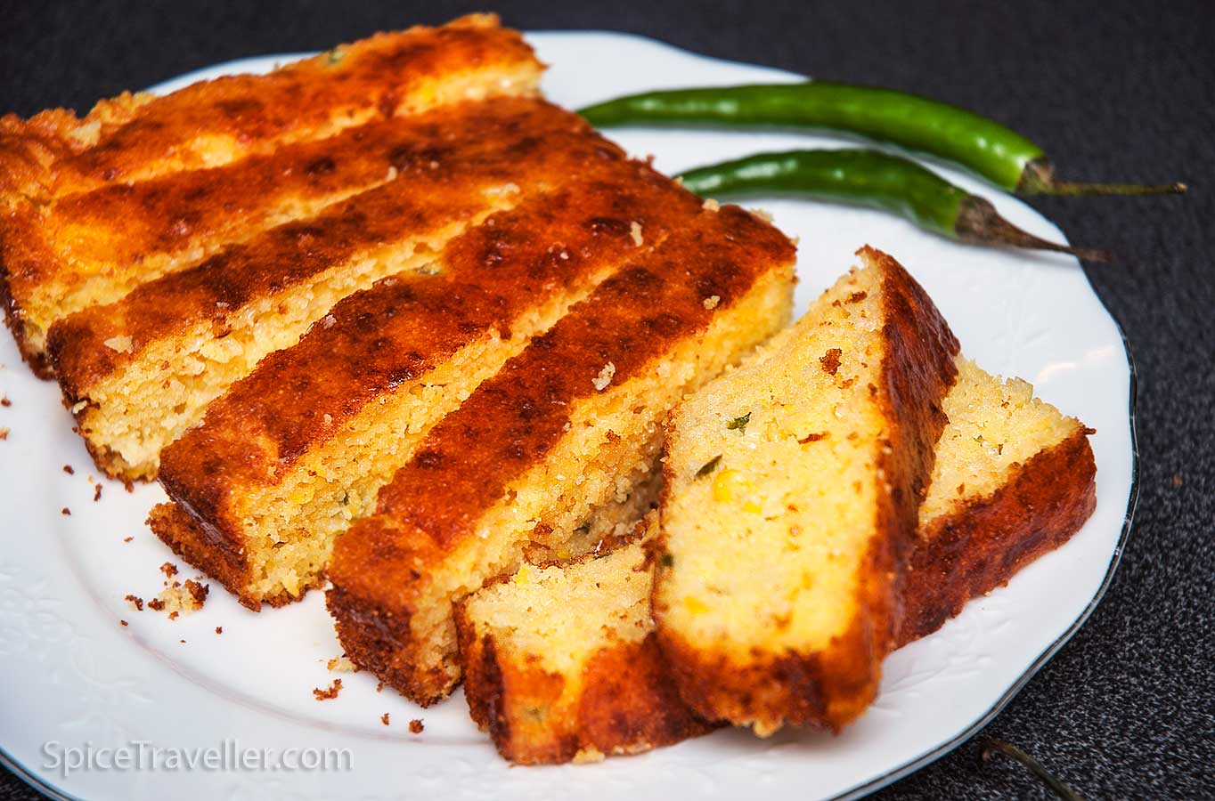 Sliced Texas corn bread on a white plate with two green chillies in the background.